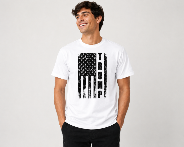A man wearing a white short-sleeve t-shirt with a distressed black American flag graphic and the word 'TRUMP' printed vertically on the front, paired with black pants, against a light gray studio background.